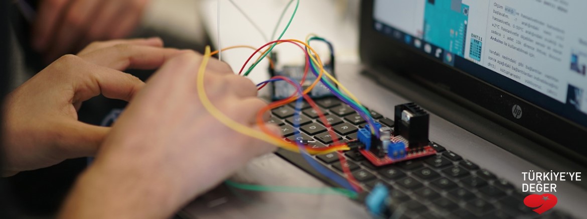 Elleri dizüstü bilgisayarda bulunan ve bilgisayarın üzerindeki kablolar ile çalışan bir kişi