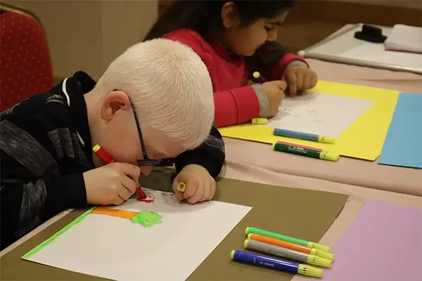 Renkli kalemlerle bir kağıt parçası üzerine çizim yapan genç bir çocuk
